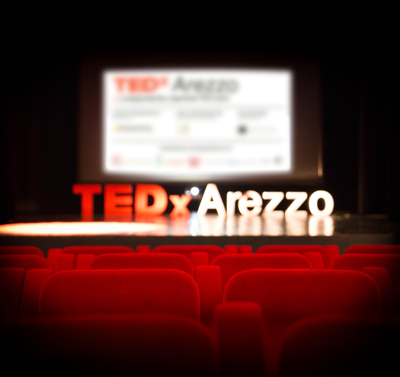 Il palco di TEDxArezzo: la scritta luminosa sul palco e le poltrone rosse della platea